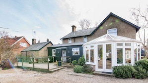 A traditional house with a conservatory, a gravel driveway, and a green fence. - Hunters Meet Ltd  (Hatfield Heath)