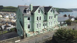 Una casa grande de color verde claro con un techo pronunciado, un porche y vistas al mar.