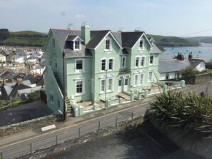 Ein großes, hellgrünes Haus mit steilem Dach, einer Veranda und Blick auf das Meer.
