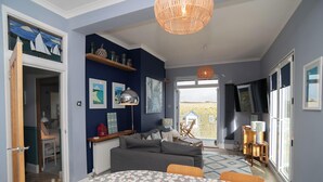 Una sala de estar acogedora con un sofá gris, un tapete estampado y un ventanal con vistas al exterior.