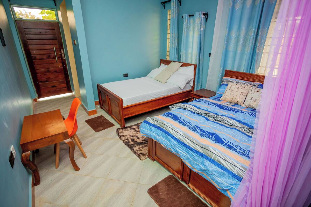 A bedroom with two beds, a wooden desk, and a chair.