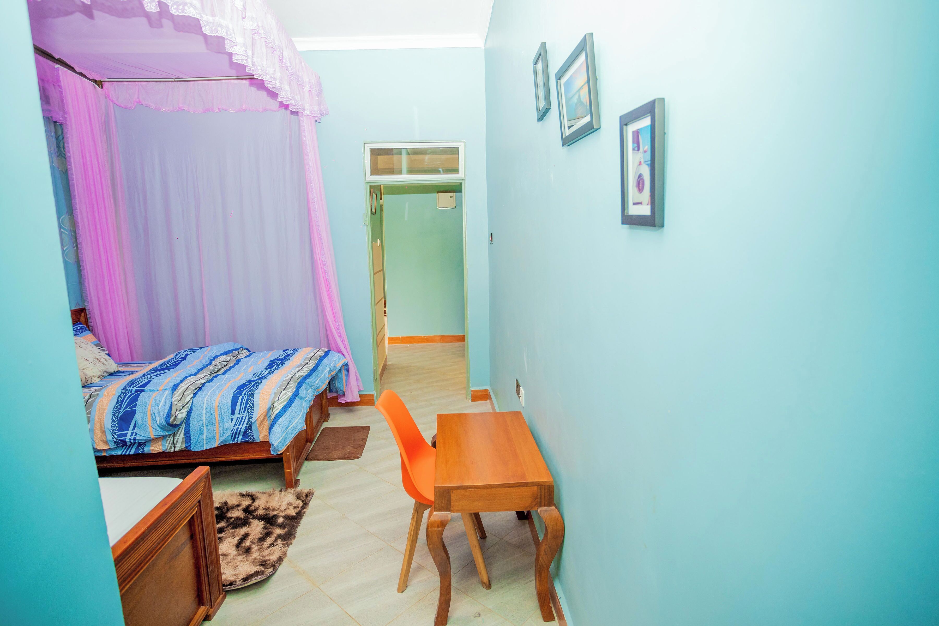 A bedroom with a bed, a wooden table, a chair, and a small rug.