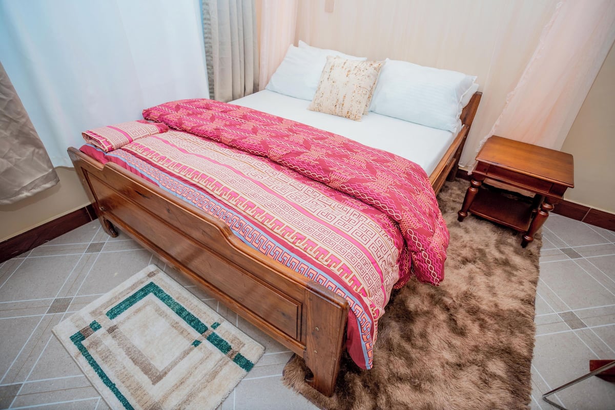 A neatly made bed with a patterned bedspread and pillows, a wooden nightstand, and a rug on the floor.