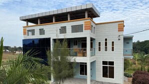 A modern two-story house with a flat roof, large windows, and a covered outdoor area. - Volunteer Hostel (Moshi)