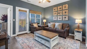 A living room with a ceiling fan, two sofas, a coffee table, a rug, and wall art. - Crossroads Vistas - 3bdr Condo (Branson)