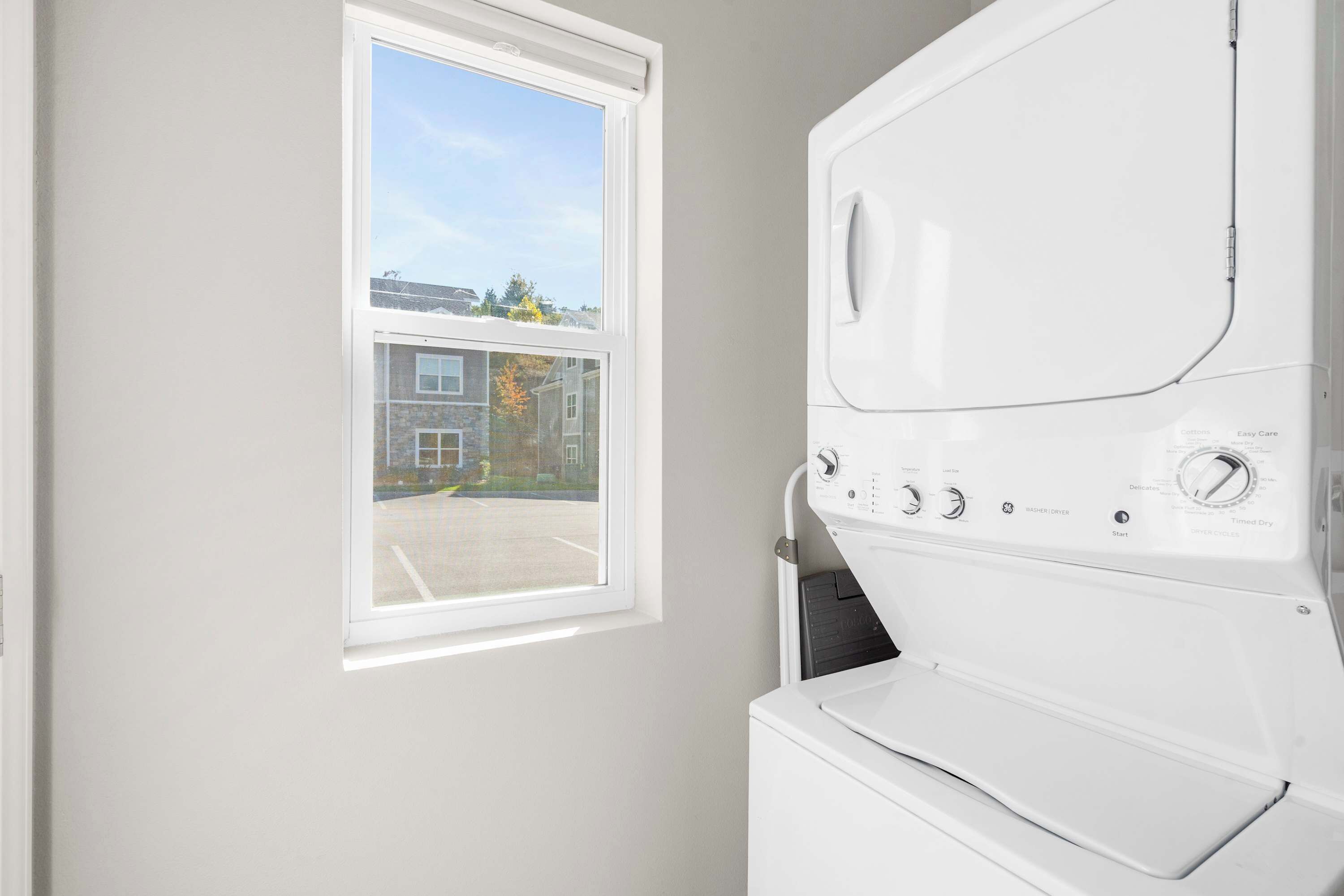 Un lavadero con una lavadora blanca, una ventana y vistas a una zona residencial.