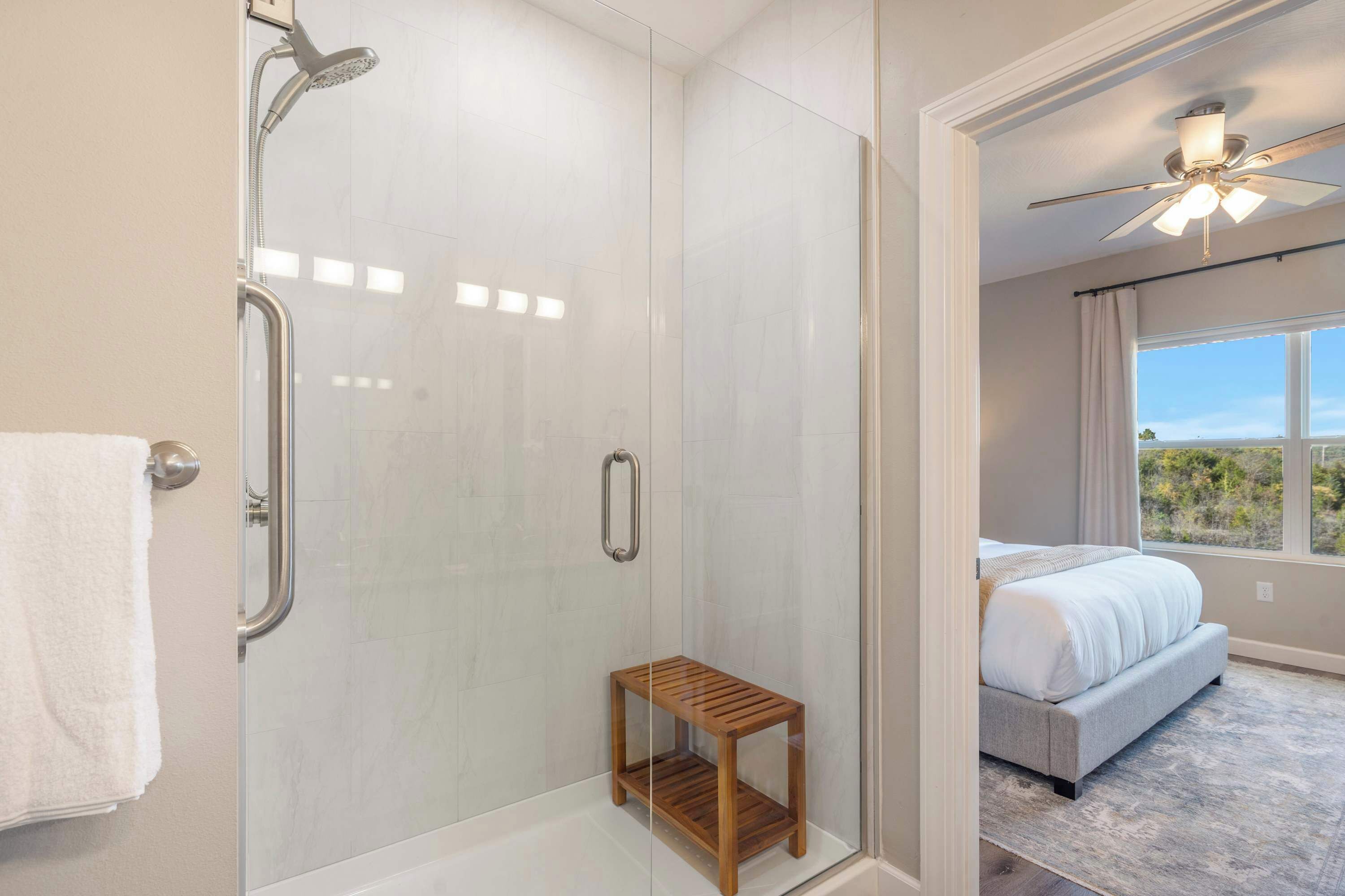 A modern bathroom with a glass shower enclosure, a small wooden stool, and a visible towel rack.