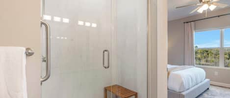 A modern bathroom with a glass shower enclosure, a small wooden stool, and a visible towel rack.