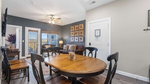 A dining area with a round wooden table, six chairs, and a ceiling fan. - Crossroads Vistas - 3bdr Condo (Branson)