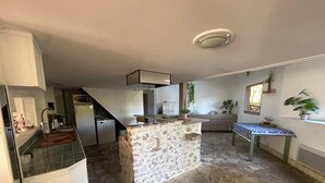 Une cuisine avec un îlot central en pierre, un coin repas avec une table et des chaises, et un petit escalier menant à un autre niveau.