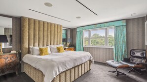 Ein modernes Schlafzimmer mit einem großen Bett, einem Ledersessel und Blick auf Grünfläche.