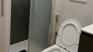 Moderni kylpyhuone, jossa on lasinen suihkuseinä, wc ja seinälle asennettu ohjauspaneeli.