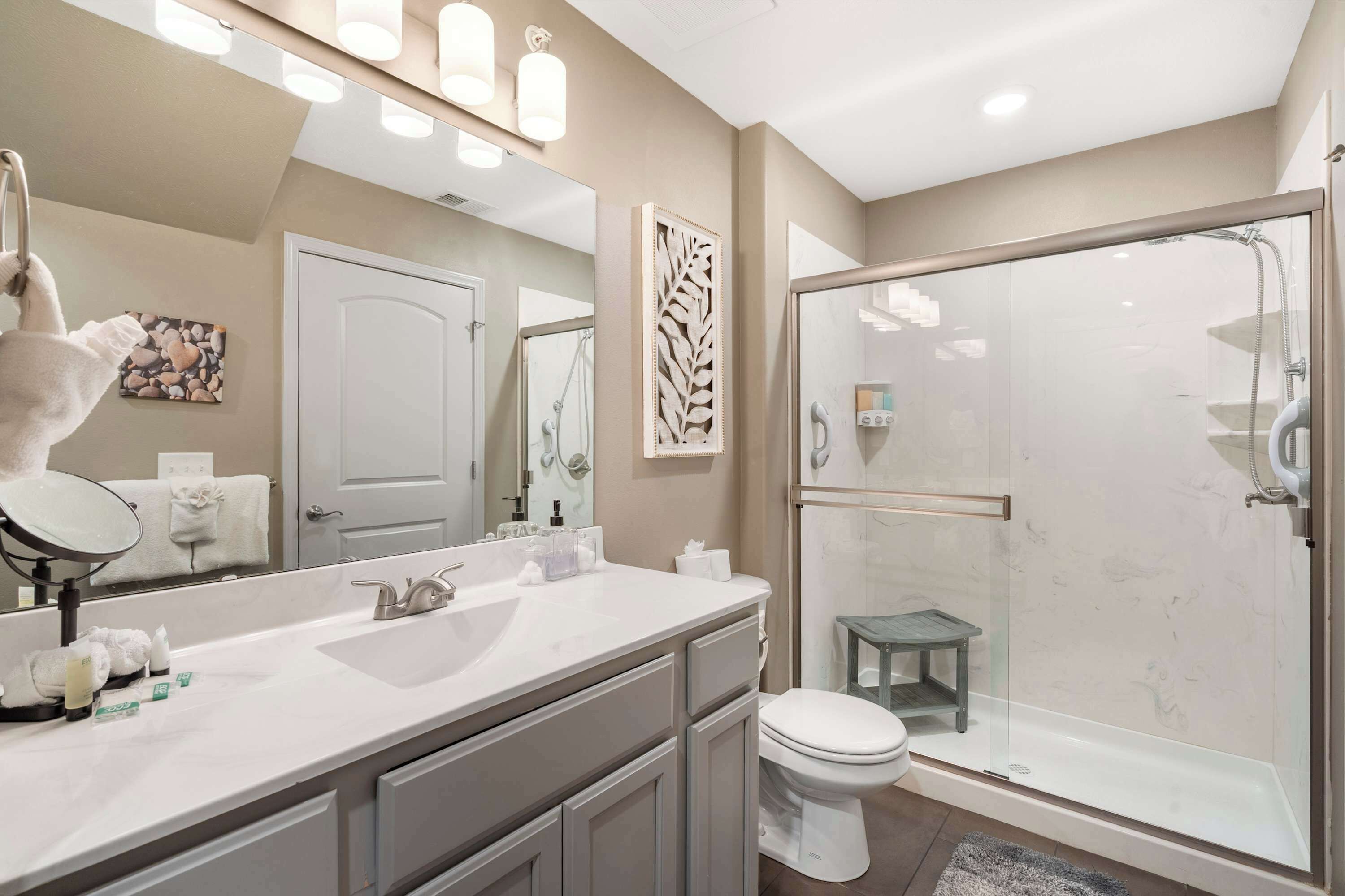 Une salle de bain moderne avec un grand miroir, un lavabo, des toilettes et une douche à parois de verre.