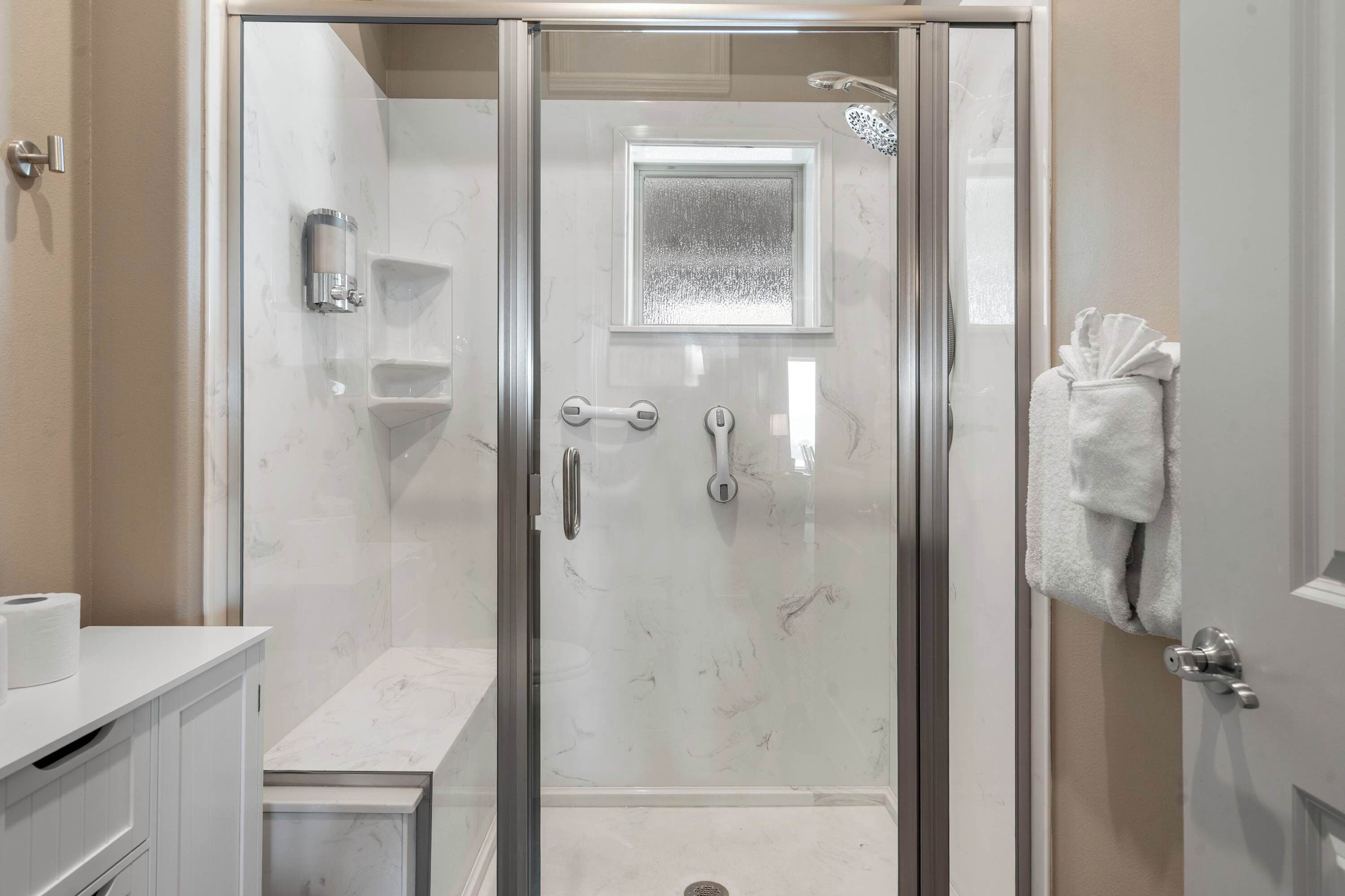 A modern bathroom with a glass-enclosed shower, a marble vanity, and a towel rack.