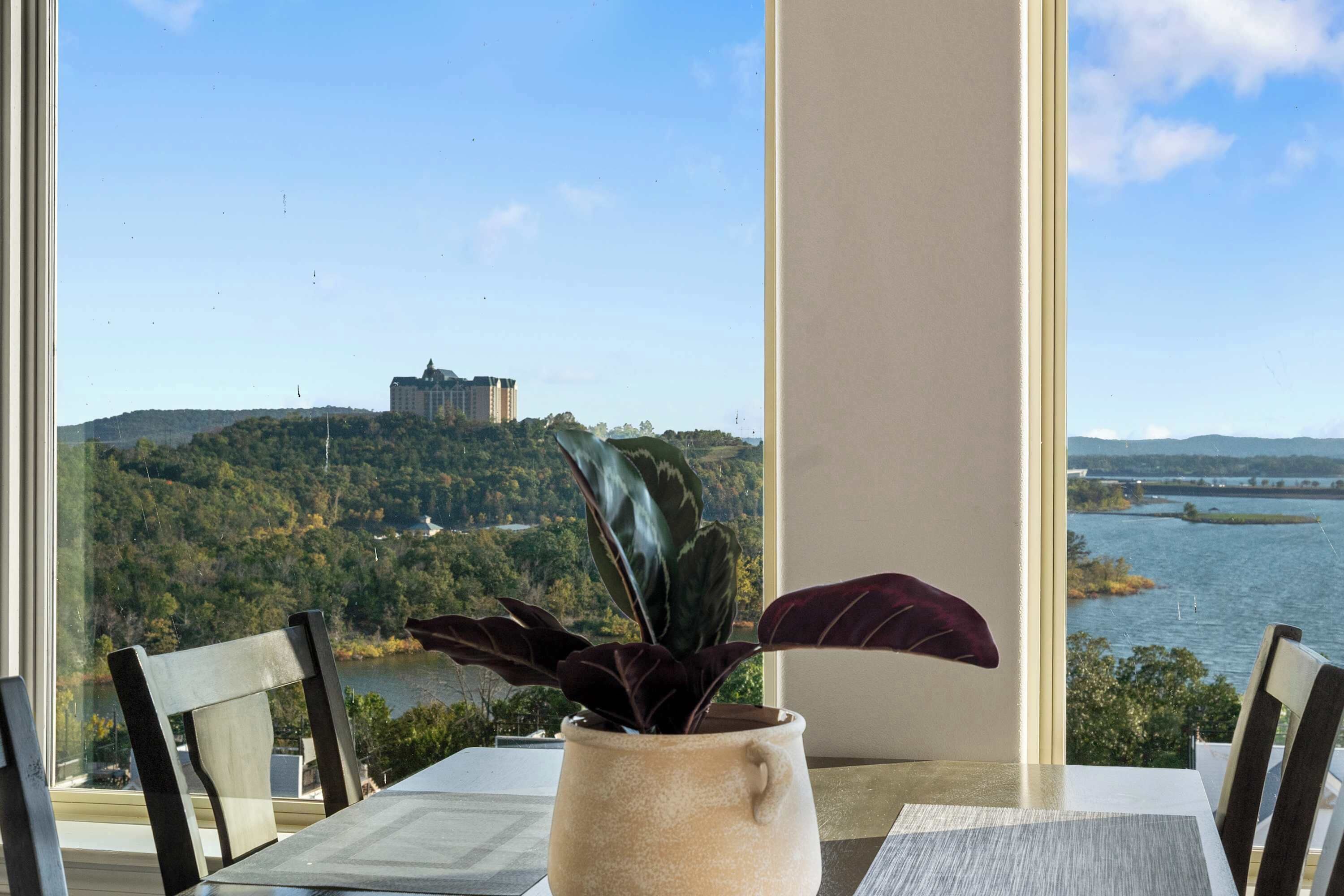 Une table avec un pot de fleurs, une fenêtre donnant sur un château et une rivière.