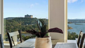 Una mesa con una planta en maceta, una ventana con vistas a un castillo y un río.