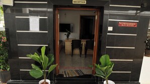 A reception area with a sign reading "RECEPTION," a desk, two chairs, and potted plants. - Aaru Residency (Coimbatore)