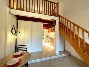 A dining area with a table and chairs, a kitchen in the background, and a wooden staircase. - Charming Duplex in the countryside (Riventosa)
