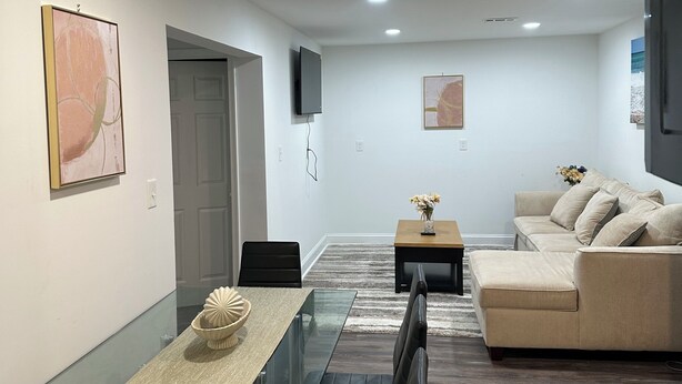 Una sala de estar moderna con una mesa de comedor de vidrio, un sofá y un televisor de pantalla plana montado en la pared.