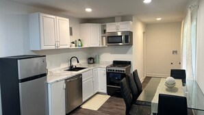 Una cocina compacta con armarios blancos, un refrigerador de acero inoxidable, un microondas, una estufa y una mesa de comedor con sillas.