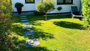 Ein Haus mit blau gefliestem Dach, ein kleiner Garten mit gepflastertem Weg und ein Stuhl.