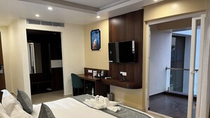 Una camera d'albergo con un letto, una scrivania, una televisione e una porta scorrevole su un balcone.