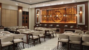 Zona pranzo di un hotel con diversi tavoli e sedie, un'ampia parete decorativa con motivi elaborati e un pavimento a fantasia.