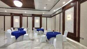 Una sala conferenze con tavoli rotondi, sedie bianche e tovaglie blu.