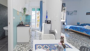 Una camera d'albergo compatta con angolo cottura, un letto con copripiumino blu e vista sul balcone esterno.
