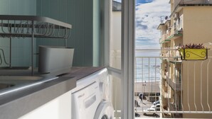 Una cucina con lavatrice, scolapiatti e vista su un balcone con ringhiera e un edificio sullo sfondo.