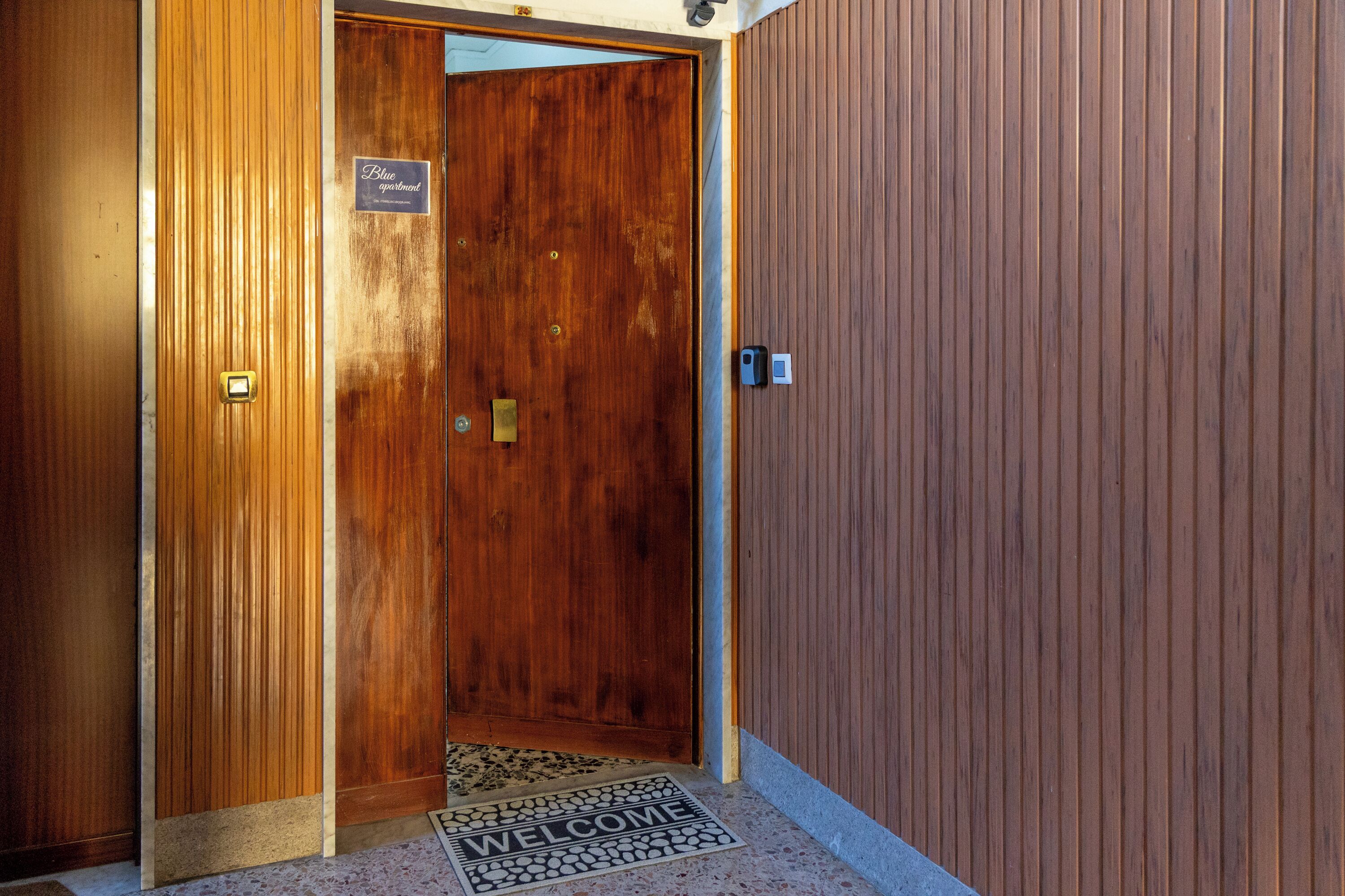 A wooden door with a welcome mat and a sign indicating a blue apartment.
