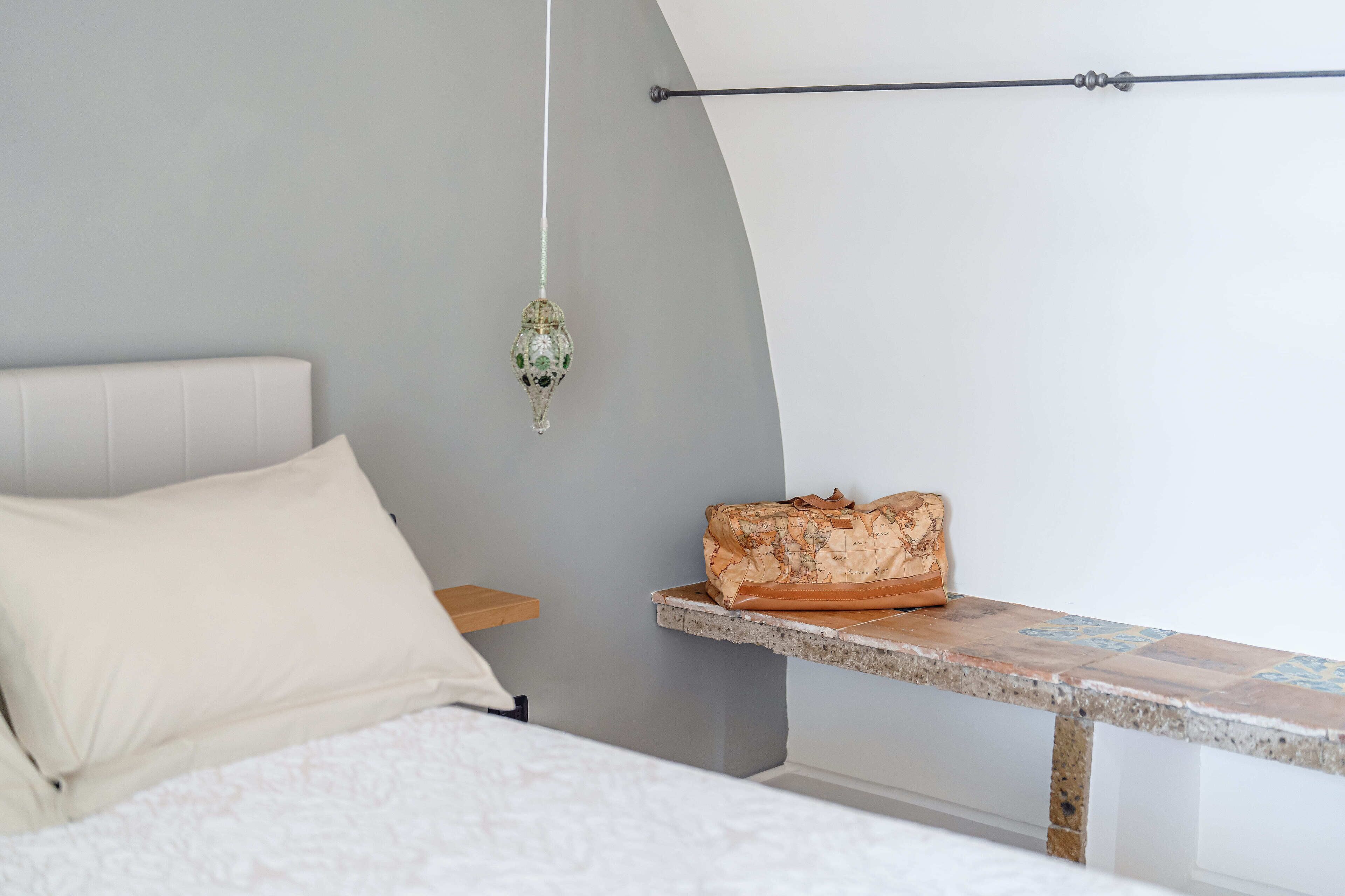 Un dormitorio con cama, lámpara colgante, banco y perchero en la pared.