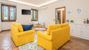Un soggiorno luminoso con divani gialli, pavimento piastrellato, televisione a schermo piatto e zona pranzo con tavolo e sedie.