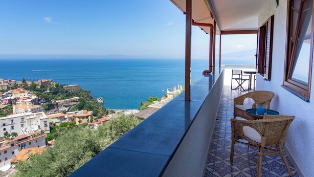 Un balcon avec vue sur la mer et la ville. On y trouve des chaises et une table en osier.