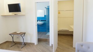 Une chambre à coucher moderne, avec un lit, une petite table, un téléviseur et une salle de bain visible à travers une porte ouverte.