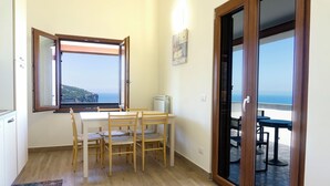 Une pièce comprenant une table à manger et des chaises, une fenêtre donnant sur la mer et une porte menant à un espace extérieur aménagé pour s’asseoir.