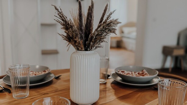 A dining table with a white vase containing dried plants, surrounded by clear glassware and plates with food remnants. - Modern apartment in Viernheim (Viernheim)