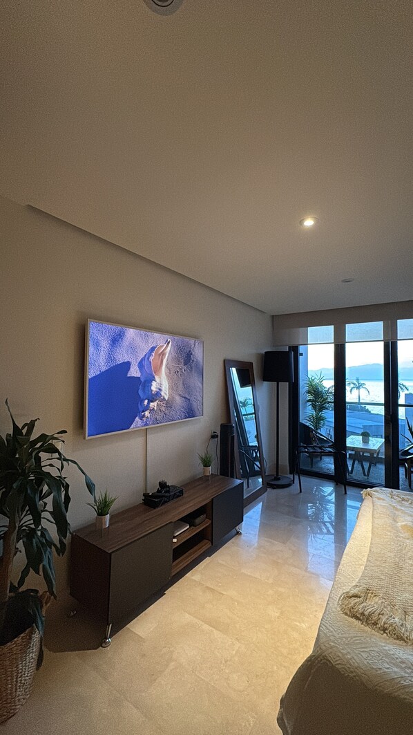 Ein modernes Schlafzimmer mit großem Fernseher, Nachttisch, Bett und Meerblick durch große Fenster.