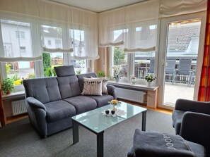 Ein modernes Wohnzimmer mit einem grauen Sofa, einem Glastisch und Blick ins Freie.