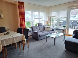 Ein modernes Wohnzimmer mit einer Couch, einem Glastisch und einem Esstisch mit Stühlen.