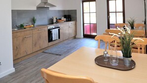 Een moderne keuken met houten kastjes, een inbouwoven en een eethoek met een tafel en stoelen.