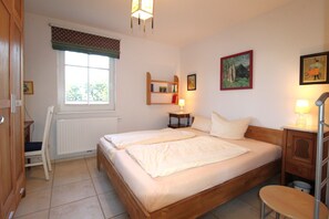 A bedroom with two single beds, a window with a view of greenery, a radiator, a bedside table with a lamp, and a small wooden cabinet. - A quiet and light-flooded vacation apartment on the first floor (Wustrow)