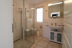 A bathroom with a glass shower enclosure, a toilet, a sink, and a mirror. - A quiet and light-flooded vacation apartment on the first floor (Wustrow)