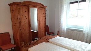 Une chambre avec une armoire en bois, un lit simple, une chaise et une fenêtre avec des rideaux.