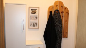 Une armoire blanche avec un seul tiroir, un tableau encadré représentant un phoque, et un porte-manteau en bois avec deux manteaux.