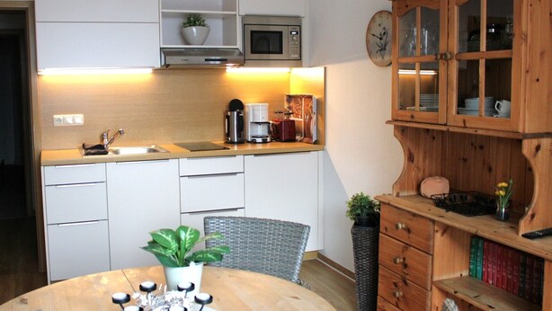 Une cuisine compacte avec des meubles blancs, un four à micro-ondes, une machine à café et un meuble en bois doté de portes en verre.
