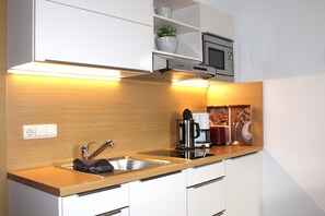 Cocina compacta con un lavabo, cafetera, microondas y una estantería con una planta.