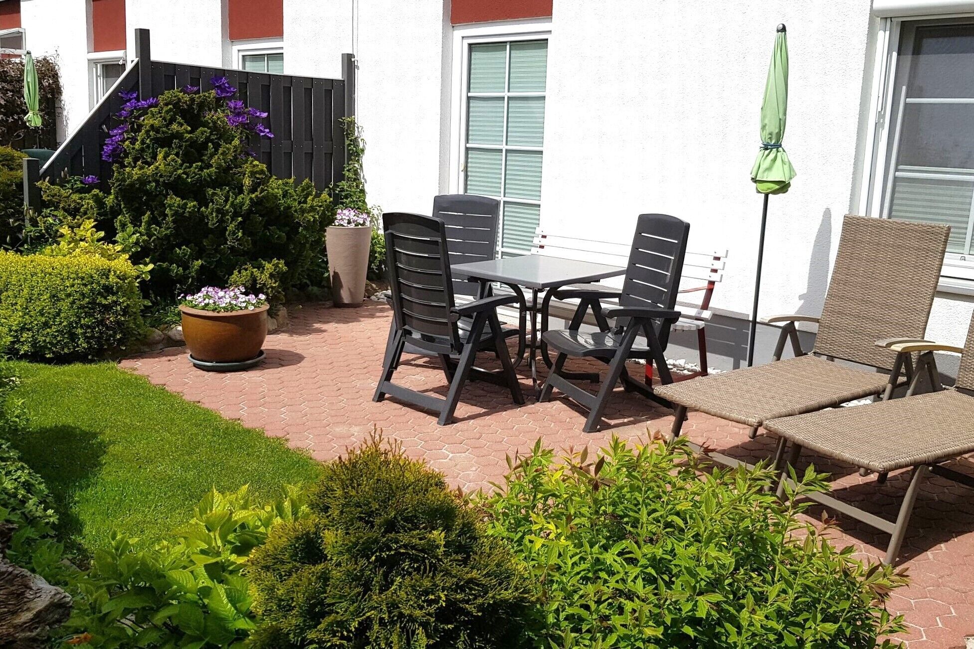 An outdoor patio with a table and chairs, surrounded by potted plants and a wooden fence.