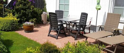 An outdoor patio with a table and chairs, surrounded by potted plants and a wooden fence.