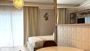Quarto de hotel moderno com uma mesa de jantar redonda, duas cadeiras laranja, uma cama, um espelho grande e um detalhe decorativo na parede.